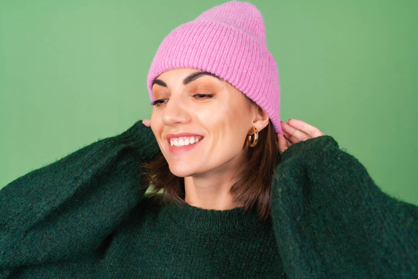Young woman on a green background in a warm cozy sweater and a pink hat cute smiling - Photo, Image