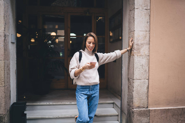 Toothy travel girl with backpack using modern mobility technology for online messaging during solo vacations, cheerful woman reading received text email and smiling connecting to international roaming - Φωτογραφία, εικόνα