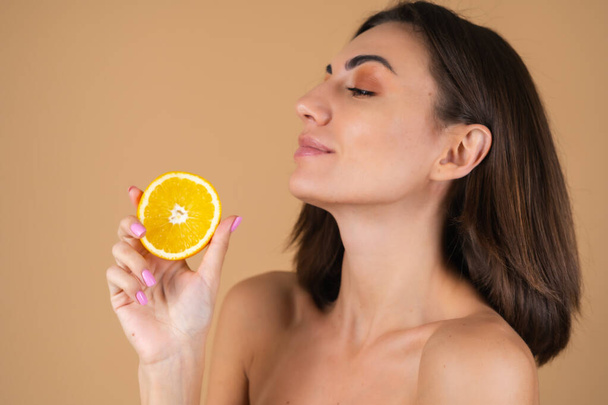 Portrait of a young woman on a beige background with natural warm make-up and smooth clean skin, holding orange circles - Foto, afbeelding