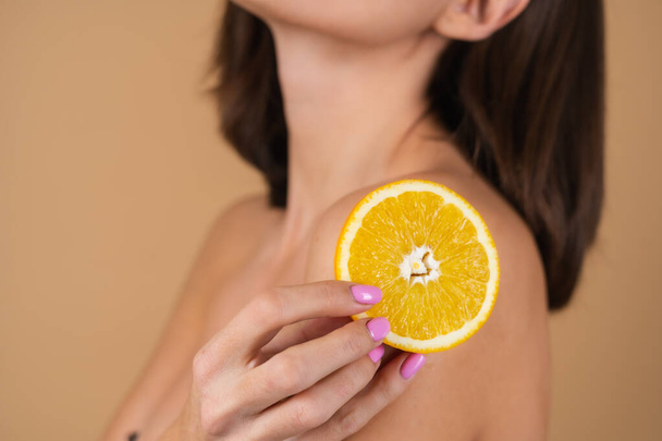 Retrato de una mujer joven sobre un fondo beige con maquillaje natural cálido y piel lisa y limpia, sosteniendo círculos naranjas - Foto, imagen