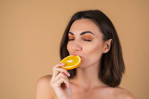 Retrato de uma jovem mulher em um fundo bege com maquiagem quente natural e pele lisa e limpa, segurando círculos laranja - Foto, Imagem