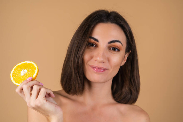 Πορτρέτο μιας νεαρής γυναίκας σε μπεζ φόντο με φυσικό ζεστό μακιγιάζ και λείο καθαρό δέρμα, κρατώντας πορτοκαλί κύκλους - Φωτογραφία, εικόνα