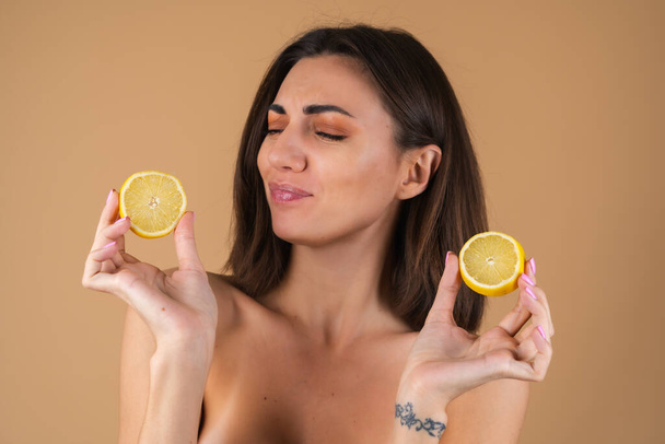 Porträt einer jungen Frau auf beigem Hintergrund mit natürlichem, warmem Make-up und glatter, sauberer Haut, die Zitronenscheiben hält - Foto, Bild