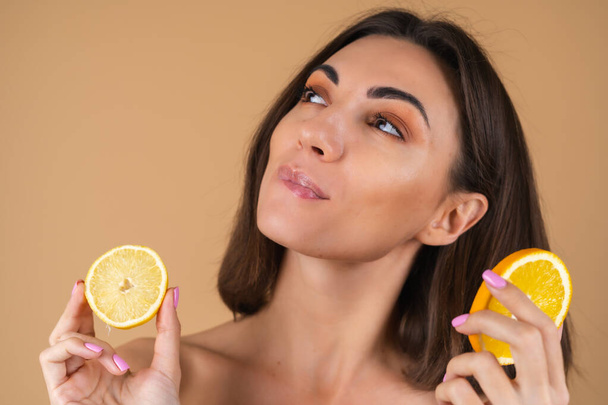 Portrait of a young woman on a beige background with natural warm make-up and smooth clean skin, holds circles of lemons and oranges - Photo, Image