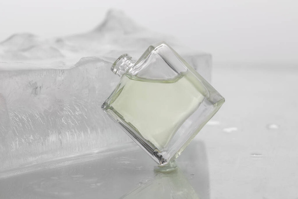 bouteille en verre de parfum vert rafraîchissant sur un fond clair avec de la glace, concept de beauté de parfum et de cosmétiques coûteux, un cadeau pour les femmes en vacances - Photo, image