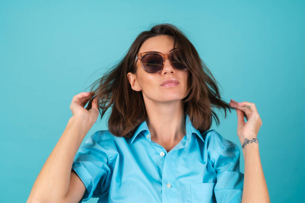 Young woman in a blue shirt on a background in sunglasses, fashionably stylish posing - Fotó, kép