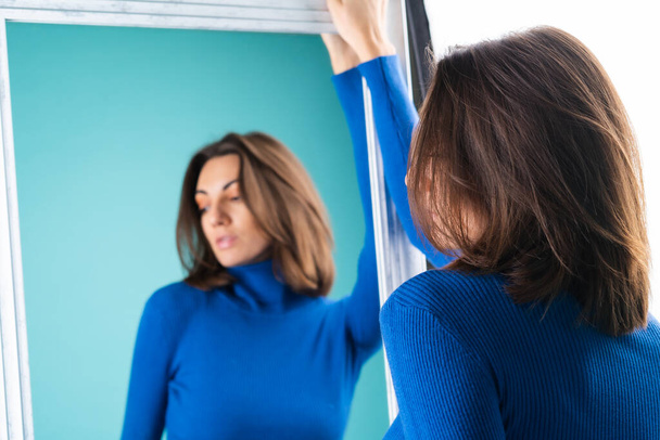 Young woman dressed in blue turtleneck, golf, posing sensually in front of the mirror - Foto, imagen