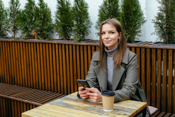 Красива усміхнена дівчина в окулярах, сидячи в кафе, тримає смартфон в руках і чіпляється
 - Фото, зображення