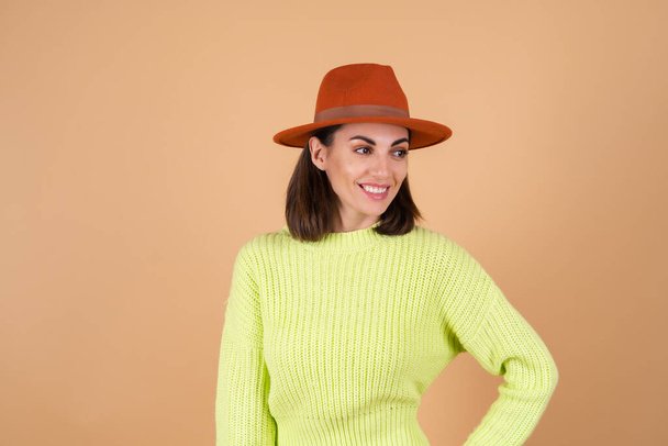 Модная стильная женщина в полный рост на бежевом фоне в брюках, свитер и шляпа смотрит в сторону, улыбаясь - Фото, изображение