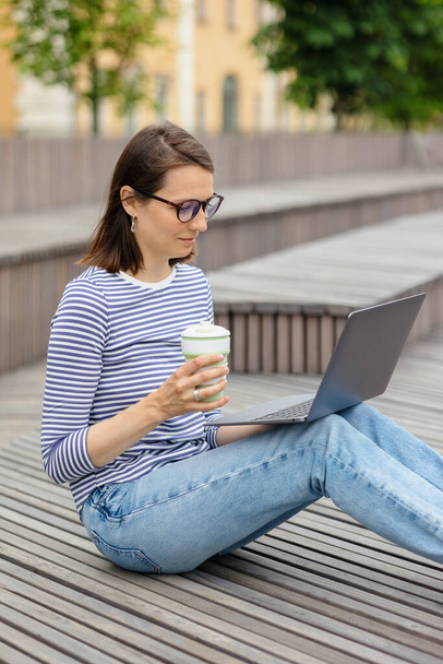 young and confident woman blogger or marketer drinking coffee and working on her laptop. work in a park or public place - Φωτογραφία, εικόνα