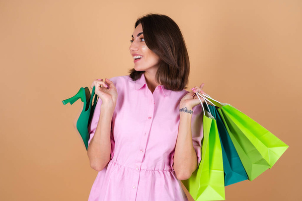 Portré egy fiatal nő rózsaszín ruhában, bézs háttér csillogó smink gazdaság cipő és bevásárló csomagok aranyos mosolygós - Fotó, kép