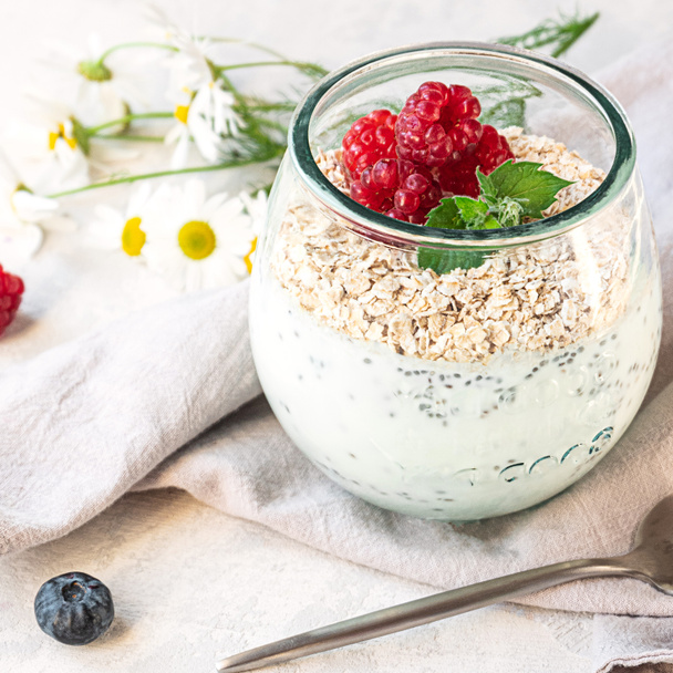 Un vaso con yogur en capas, semillas de chía, avena y bayas, mesa de hormigón gris. Desayuno saludable, concepto de estilo de vida saludable - Foto, imagen