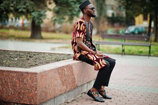 African stylish and handsome man in traditional outfit and black cap standing outdoor. - Valokuva, kuva