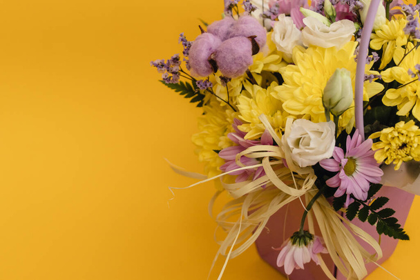 Sarı-menekşe çiçek aranjmanı bir kutu kasımpatı, Eustoma, pamuk cilt bakımı ve sarı arka planda kurumuş çiçekler. - Fotoğraf, Görsel
