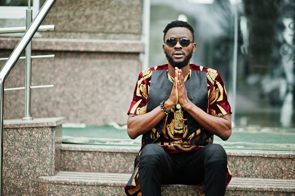 African stylish and handsome man in traditional outfit and sunglasses pray outdoor. - Foto, immagini