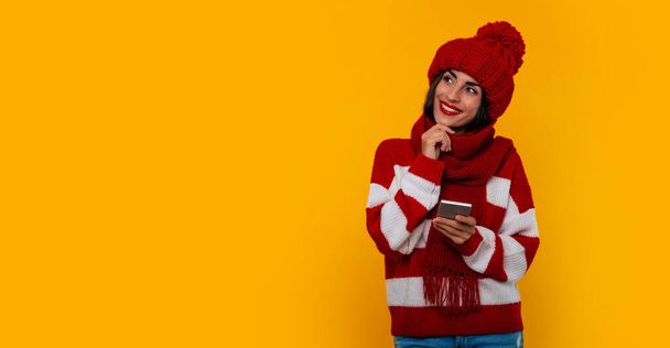 彼女は彼女のスマートフォンを使用しながら、幸せと興奮若い現代美しい女性の肖像画で赤い冬の帽子とスカーフ - 写真・画像