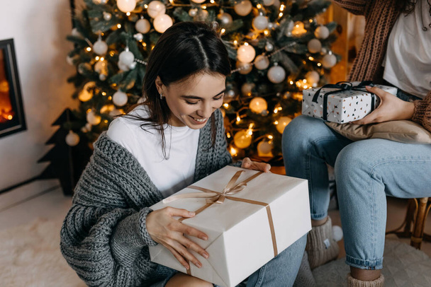 fiatal barna nő kezében egy ajándék, ül a karácsonyfa háttér. - Fotó, kép