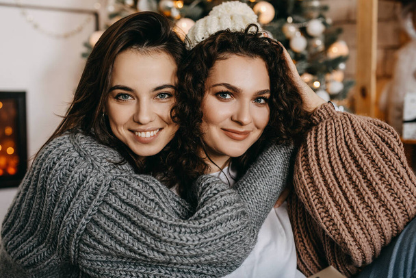 Due giovani donne brune felici sullo sfondo dell'albero di Natale, abbracciando, sorridendo, guardando la macchina fotografica. - Foto, immagini