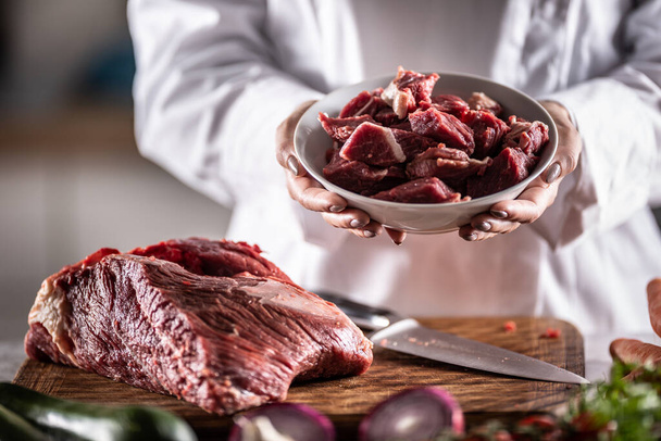 Small chunks of beef or pork for stew in a bowl next to a large piece of red meat on a cutting board. - Photo, image