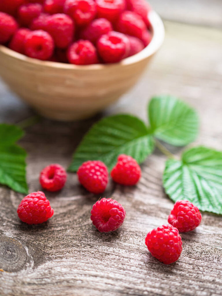 Fresh ripe red raspberries with leaves in a bowl on rustic old wooden table. Healthy organic food, summer vitamins, BIO viands, natural background. Copy space for your advertising text message. - Fotografie, Obrázek