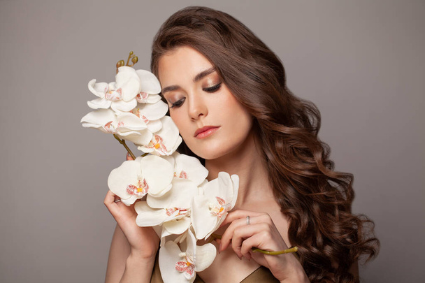 Ελκυστική γυναίκα με μακριά τέλεια σγουρά μαλλιά και λευκά λουλούδια, πορτρέτο μόδας - Φωτογραφία, εικόνα