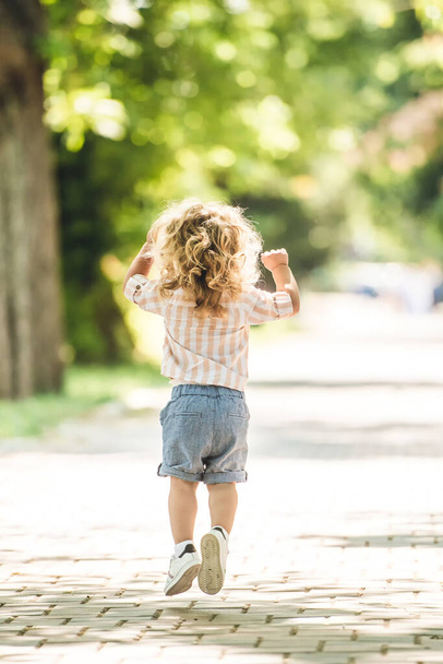 Cute little boy with curly blonde hair playing in park - 写真・画像