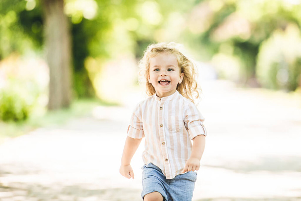 Cute little boy with curly blonde hair playing in park - Foto, Imagen
