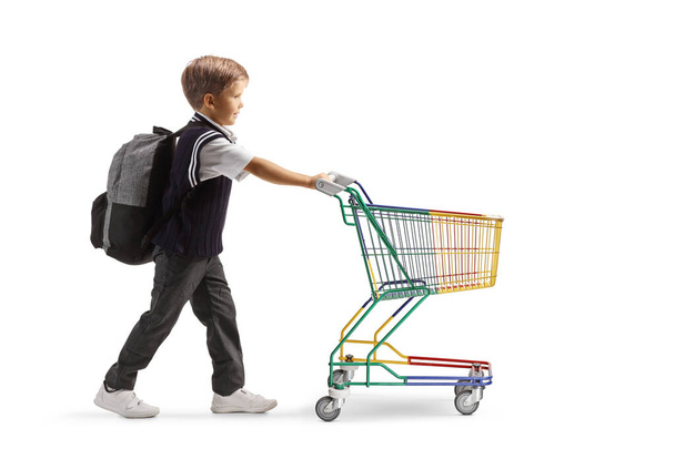 Teljes hossz profilkép egy iskolás fiú nyomja egy mini bevásárlókocsi elszigetelt fehér backgroun - Fotó, kép