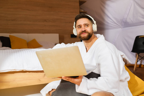 Homem barbudo bonito jovem com fones de ouvido e laptop - Foto, Imagem