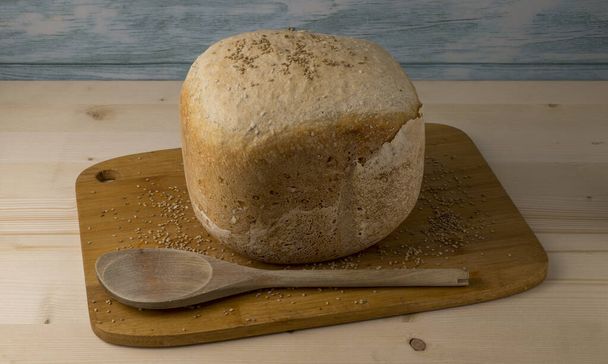Pão de gergelim recém-assado em uma tábua de corte. Pão macio caseiro com concha de madeira - Foto, Imagem