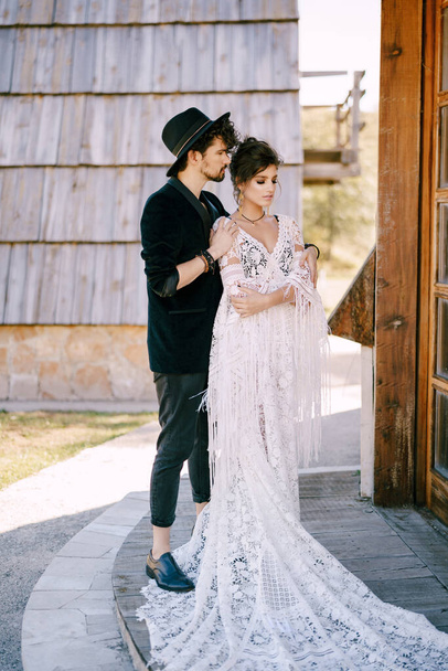 Наречена обіймає наречену в мереживному плетеному платті на порозі дерев'яної хатини
 - Фото, зображення