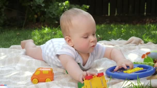 Aranyos baba mászik a füvön, hogy színes játékok. A gyermekek korai fejlődésének, oktatásának és kikapcsolódásának koncepciója a szabadban. - Felvétel, videó