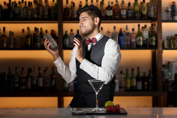 Ο γαμάτος επαγγελματίας μπάρμαν φτιάχνει κοκτέιλ, κουνάει ένα σέικερ. Αυθεντικός μπάρμαν που φτιάχνει αλκοολούχα ποτά σε μοντέρνο μπαρ. - Φωτογραφία, εικόνα
