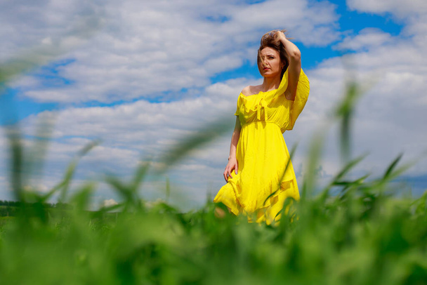 Mujer joven con un vestido amarillo al aire libre en un campo verde. Felicidad de estar en la naturaleza con buena ecología. - Foto, Imagen