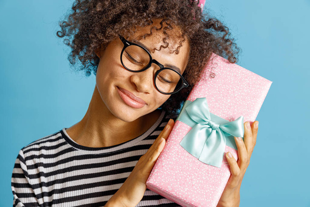 Joyful multiethnic woman holding gift box with ribbon - 写真・画像