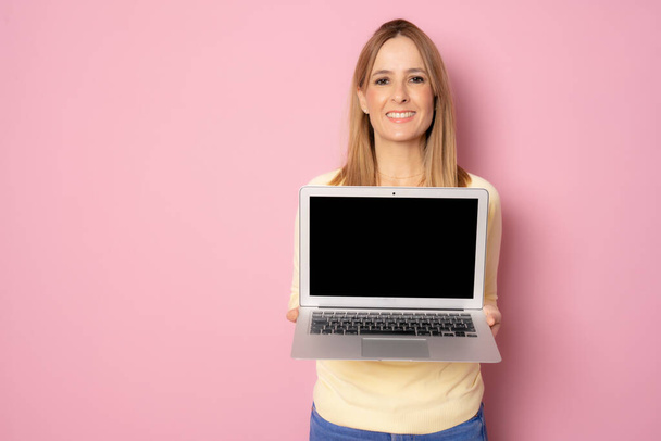 Νεαρή χαμογελαστή γυναίκα φορώντας casual ρούχα οθόνη του φορητού υπολογιστή στέκεται απομονωμένη σε ροζ φόντο. - Φωτογραφία, εικόνα