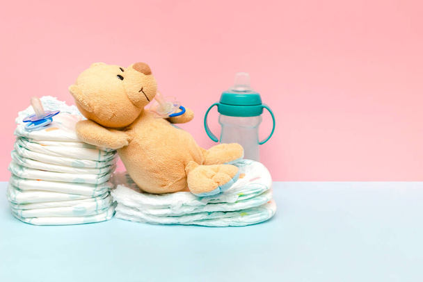 Een stapel luiers met schattige teddybeer speelgoedfopspeen op tafel. set voor baby pasgeboren jongen meisje voor baby shower cadeau op blauw roze achtergrond kopiëren ruimte. Gezondheidszorg medisch, hygiëne concept - Foto, afbeelding