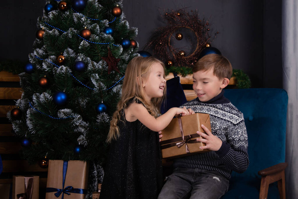 Χαρούμενα παιδιά που παίζουν με χριστουγεννιάτικα δώρα. αδέλφια κοντά στο χριστουγεννιάτικο δέντρο δίνοντας δώρα για το νέο έτος ο ένας στον άλλο. Οικογενειακή ώρα. Τα αδέλφια αγαπούν. - Φωτογραφία, εικόνα
