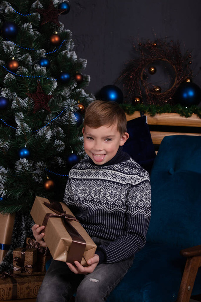 boldog jóképű csinos tinédzser szőke fiú kötött pulóverben gazdaság új év ajándék közelében egy karácsonyfa - Fotó, kép