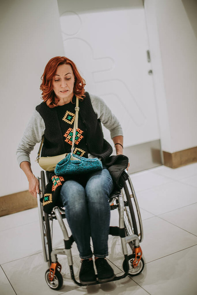 Eine Frau im Rollstuhl in der Nähe einer Toilettentür mit einem Toilettenschild für Menschen mit Behinderungen. Öffentliche Toilette im Einkaufszentrum, zugänglich für Personen jeden Geschlechts. Selektiver Fokus. - Foto, Bild