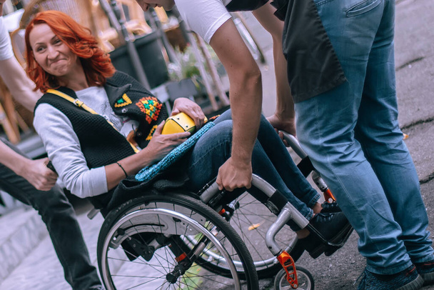 girl in a wheelchair is carried up the stairs to the cafe. Inaccessible to people with special needs, public places without ramps. Selective focus. - Photo, Image