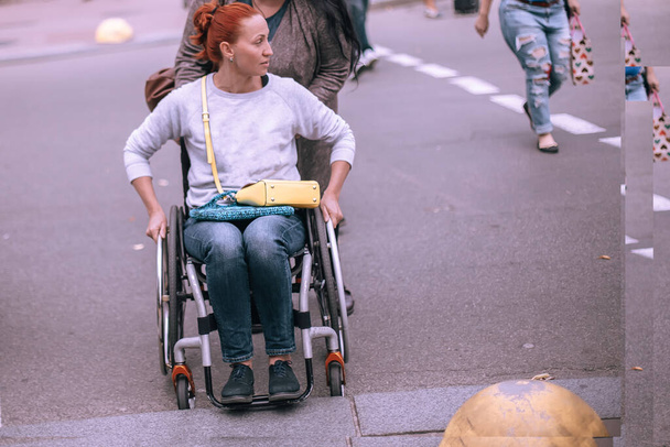 жінка допомагає дівчині в інвалідному візку увійти в рампу на пішохідному переході в місті. Доступне місто для людей з особливими потребами. Люди в дорозі. Вибірковий фокус
. - Фото, зображення