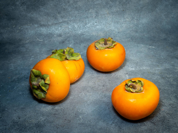 Four persimmons on a black background. Persimmon varieties Chamomile. still life. Big ripe tasty fruits on the table.  - Foto, Bild