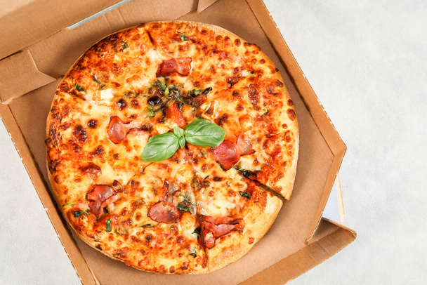 Pizza ronde cuite au four dans une boîte artisanale sur un fond de ciment gris clair, vue de dessus gros plan. - Photo, image