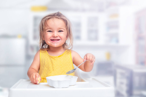 schattig kind meisje eten cornflakes met melk in baby voedende stoel - Foto, afbeelding