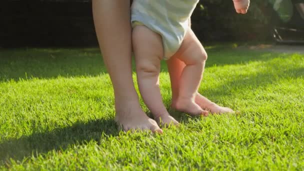 Close-up van blootsvoets baby met moeder staan op vers groen gras gazon in huis achtertuin. Begrip gezonde levensstijl, ontwikkeling van kinderen en ouderschap. - Video