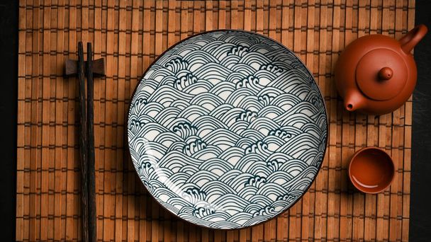 Placa cerámica de porcelana asiática con palillos y set de té en mantel de bambú. vista superior, plano - Foto, imagen