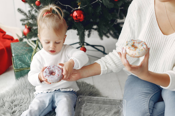 Mother with little daughter sitting near Christmas tree and and go donuts. - Foto, Imagem