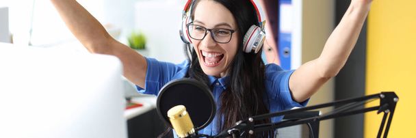 Mulher sorridente em fones de ouvido se alegrando na frente do microfone na estação de rádio - Foto, Imagem