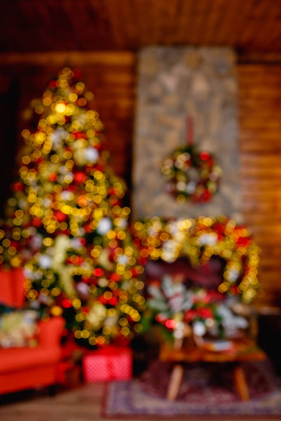 Rozostřený obraz. Červená a zlatá dekorace na vánočním stromečku v pokoji s křeslem a krbem. rozmazané pozadí fotografie s bokeh světla z girlands. - Fotografie, Obrázek